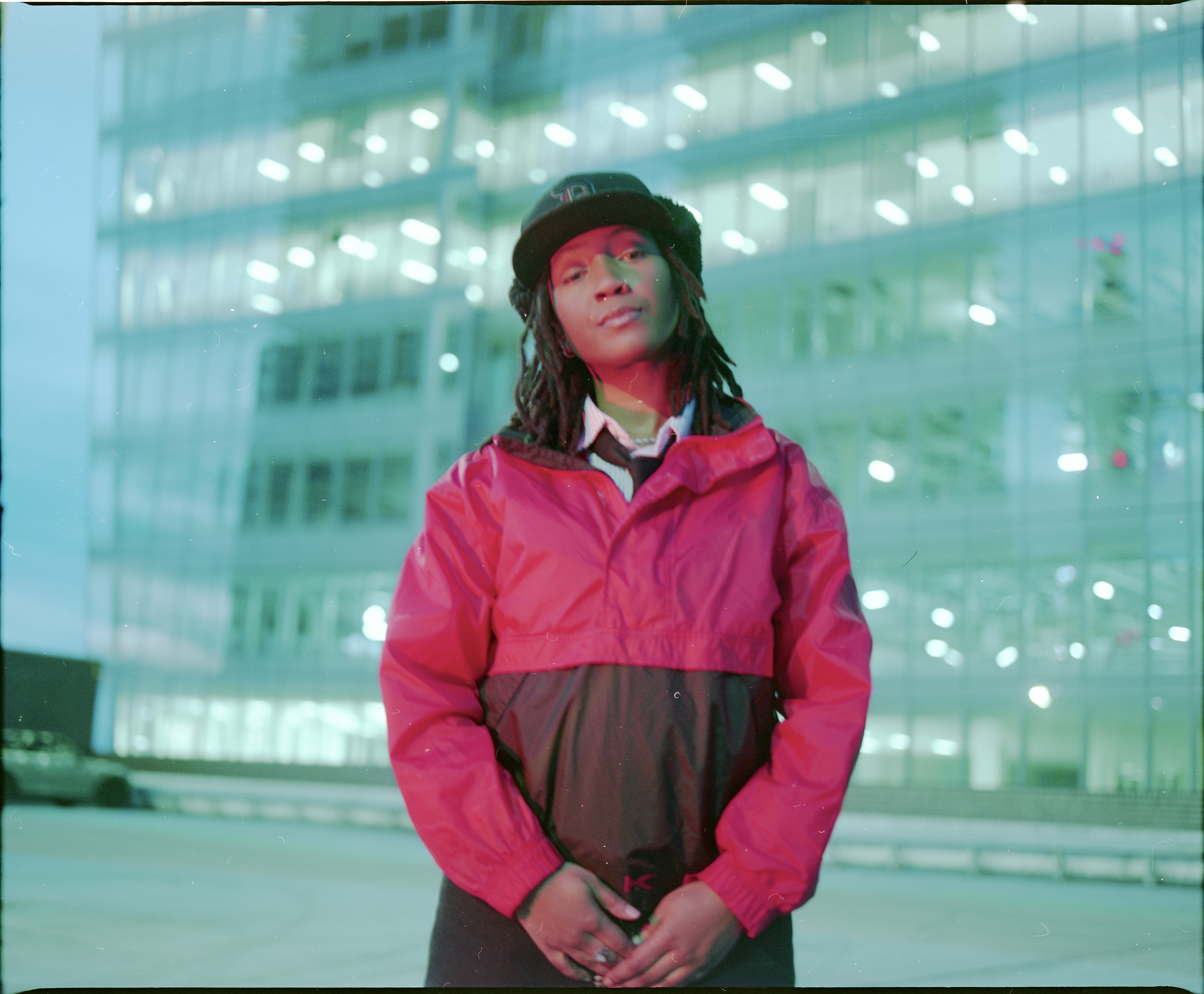 a photo taken by Connor of a person standing wearing a pink jacket and a bucket hat with a building in the background