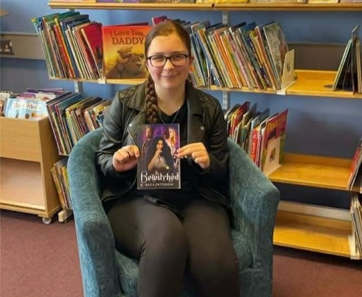 kaila sitting in a chair holding her book Bewitched
