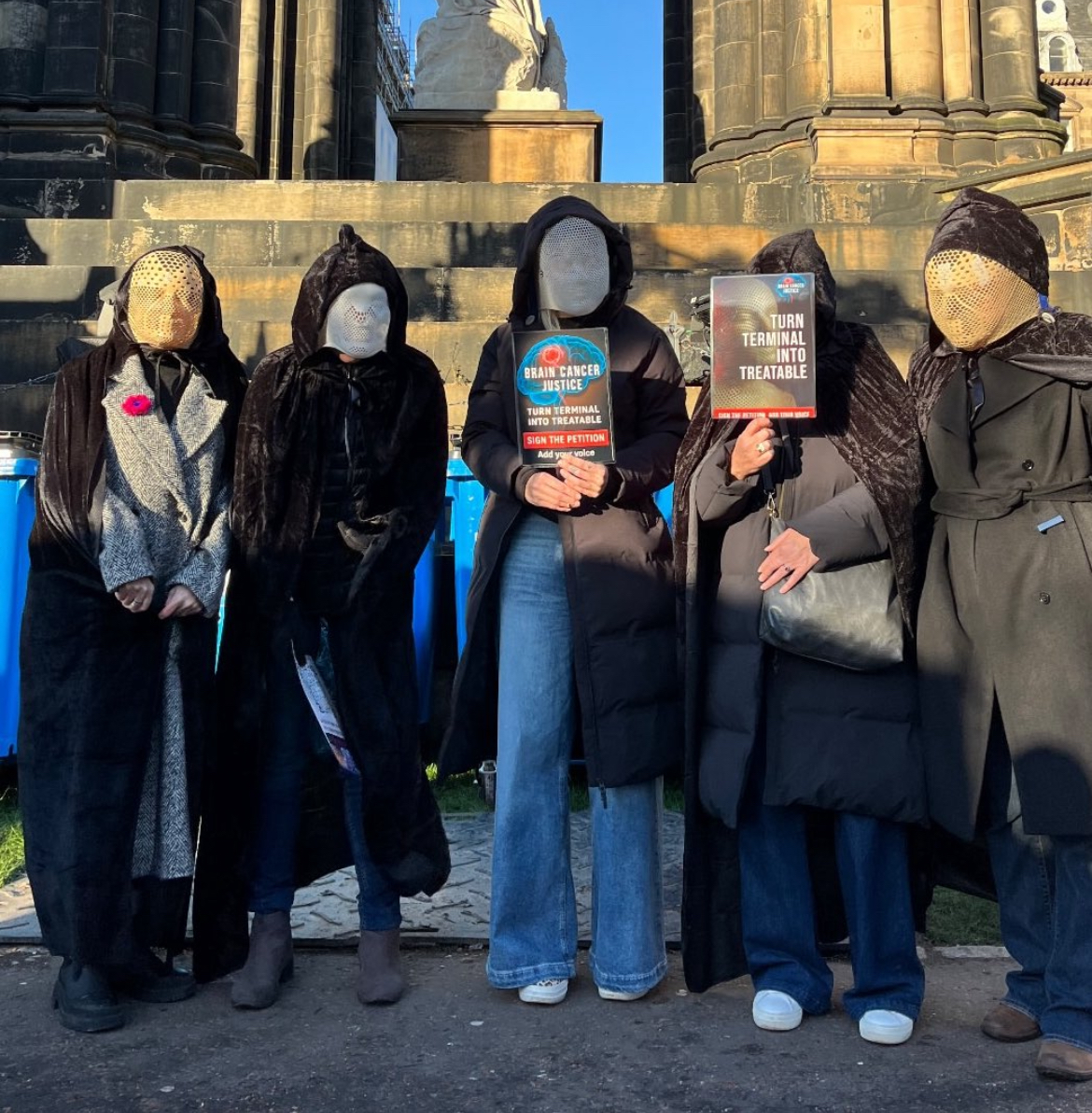 The Brain Banshees dressed in black cloaks and radiotherapy masks in Edinburgh, Scotland