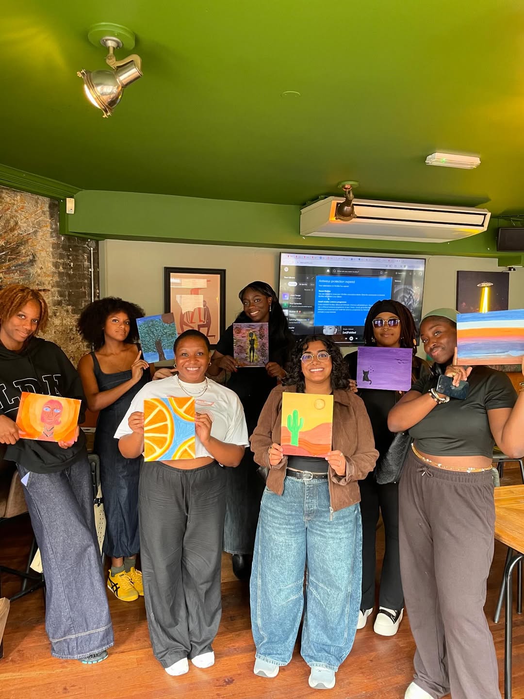 group of young women from Fourth Root smiling at the camera holding up paintings