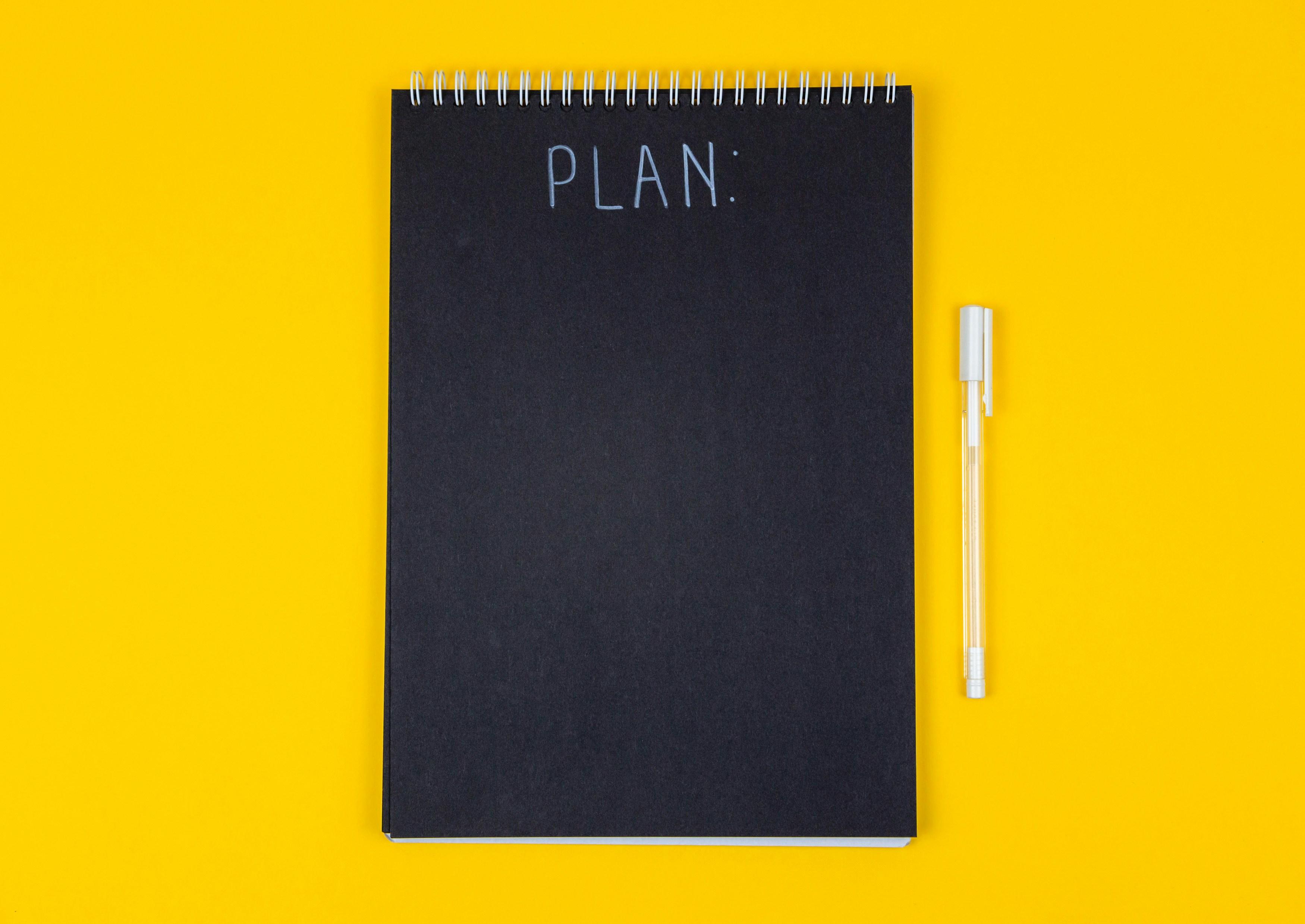 a black notebook that says "Plan" on a yellow background