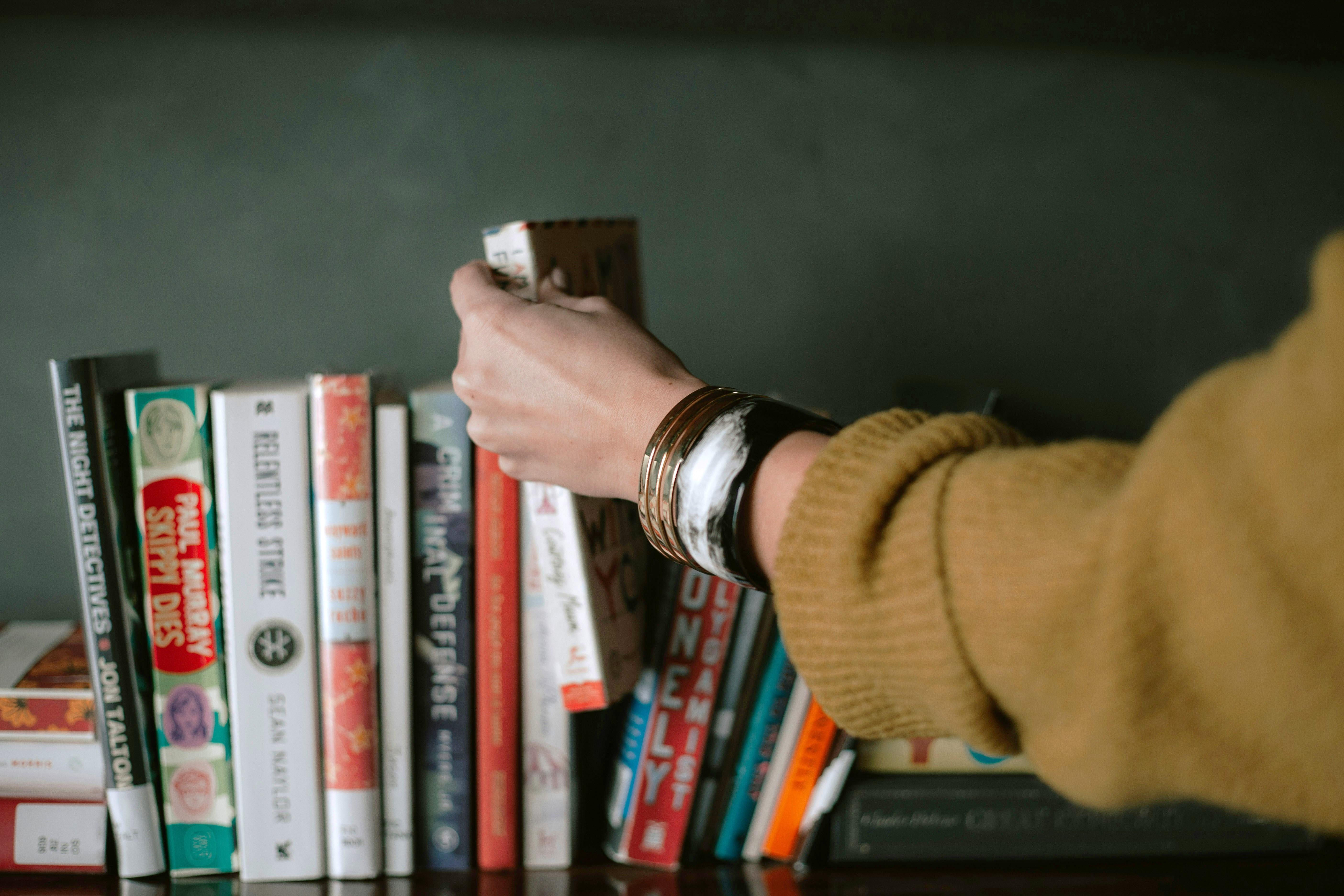 person picking a book from a bookshelf