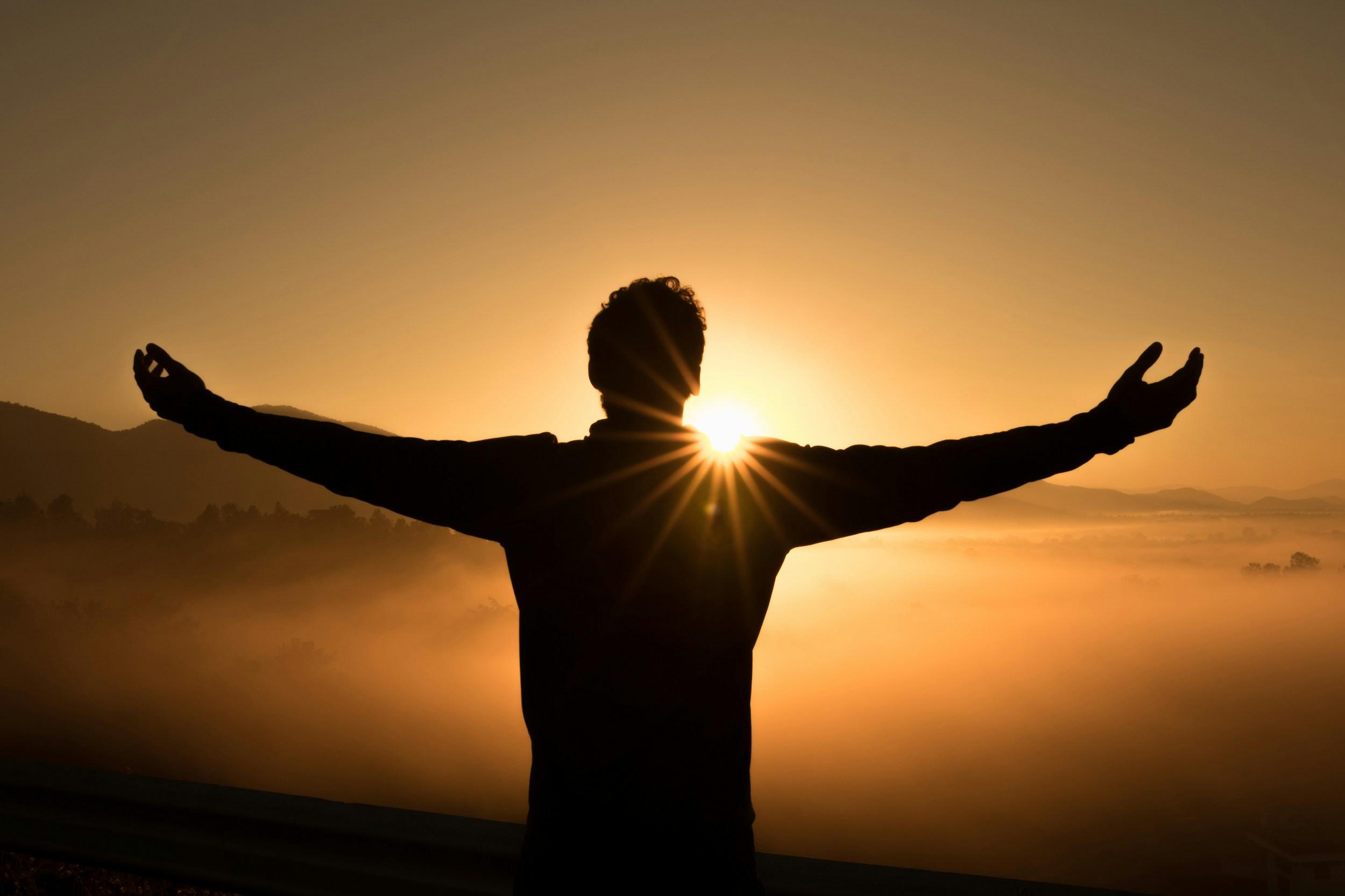 man standing with his arms stretched out at sunset