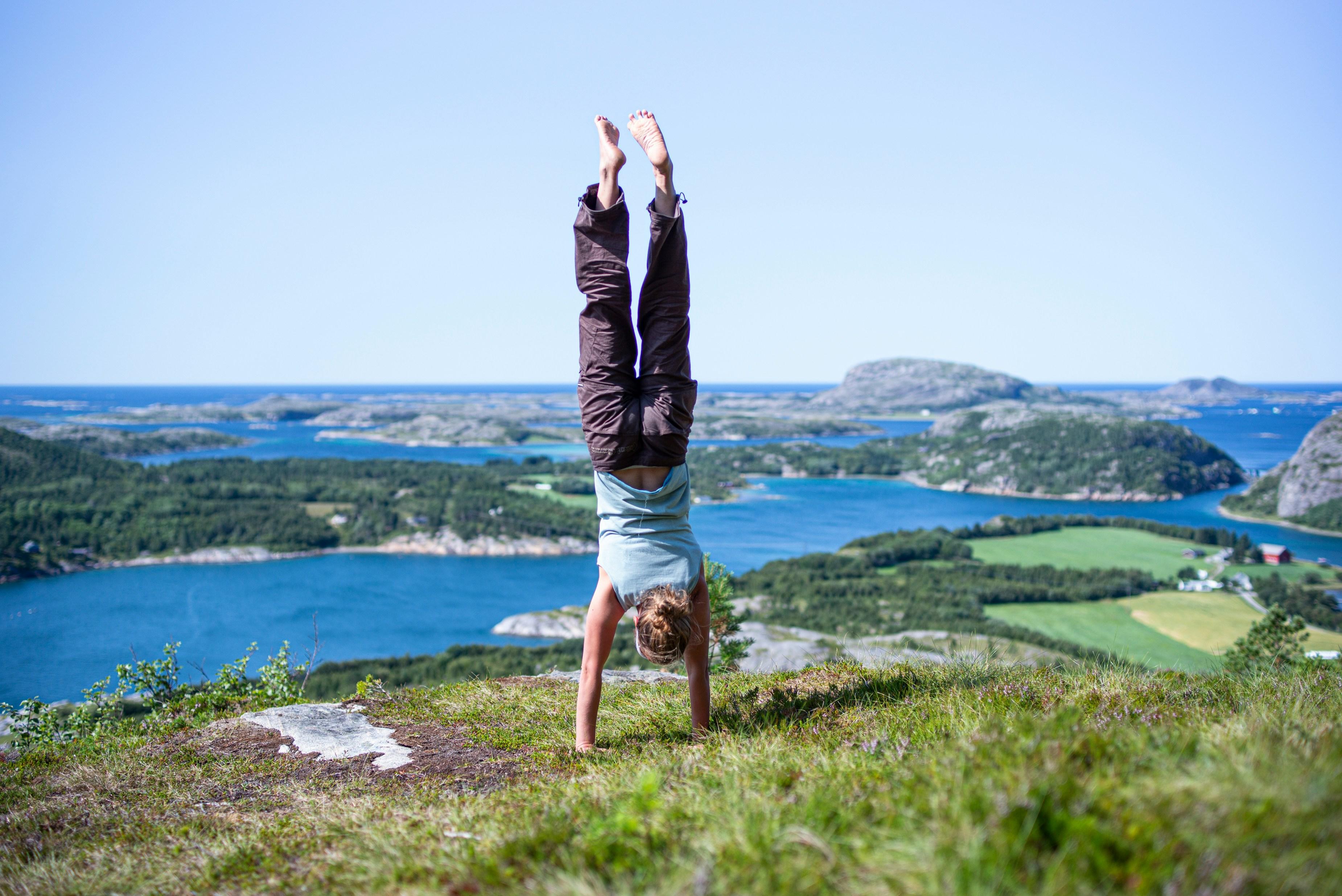 person doing a handstand on a hill overlooking water