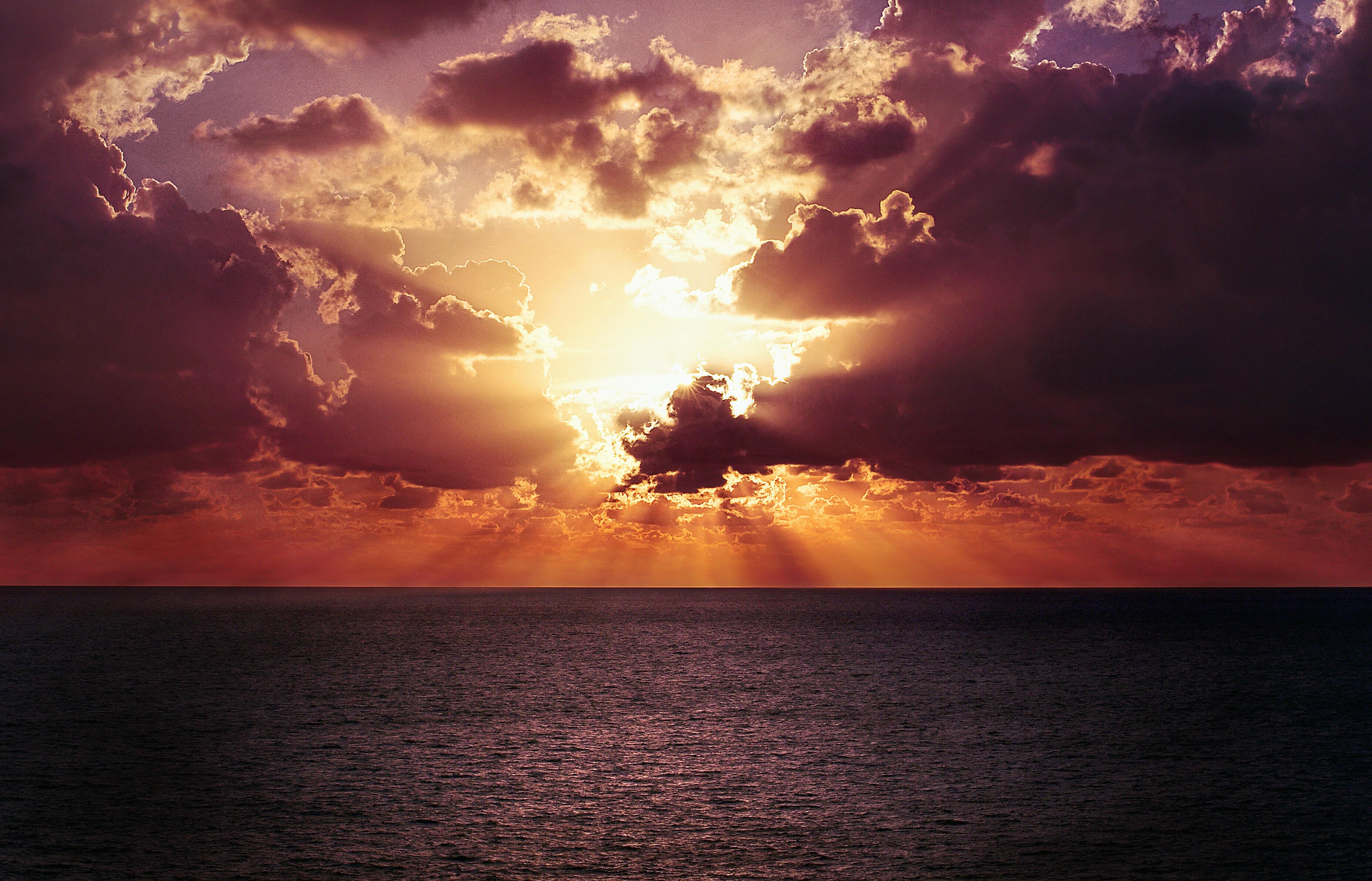 sun peaking through the clouds over a body of water