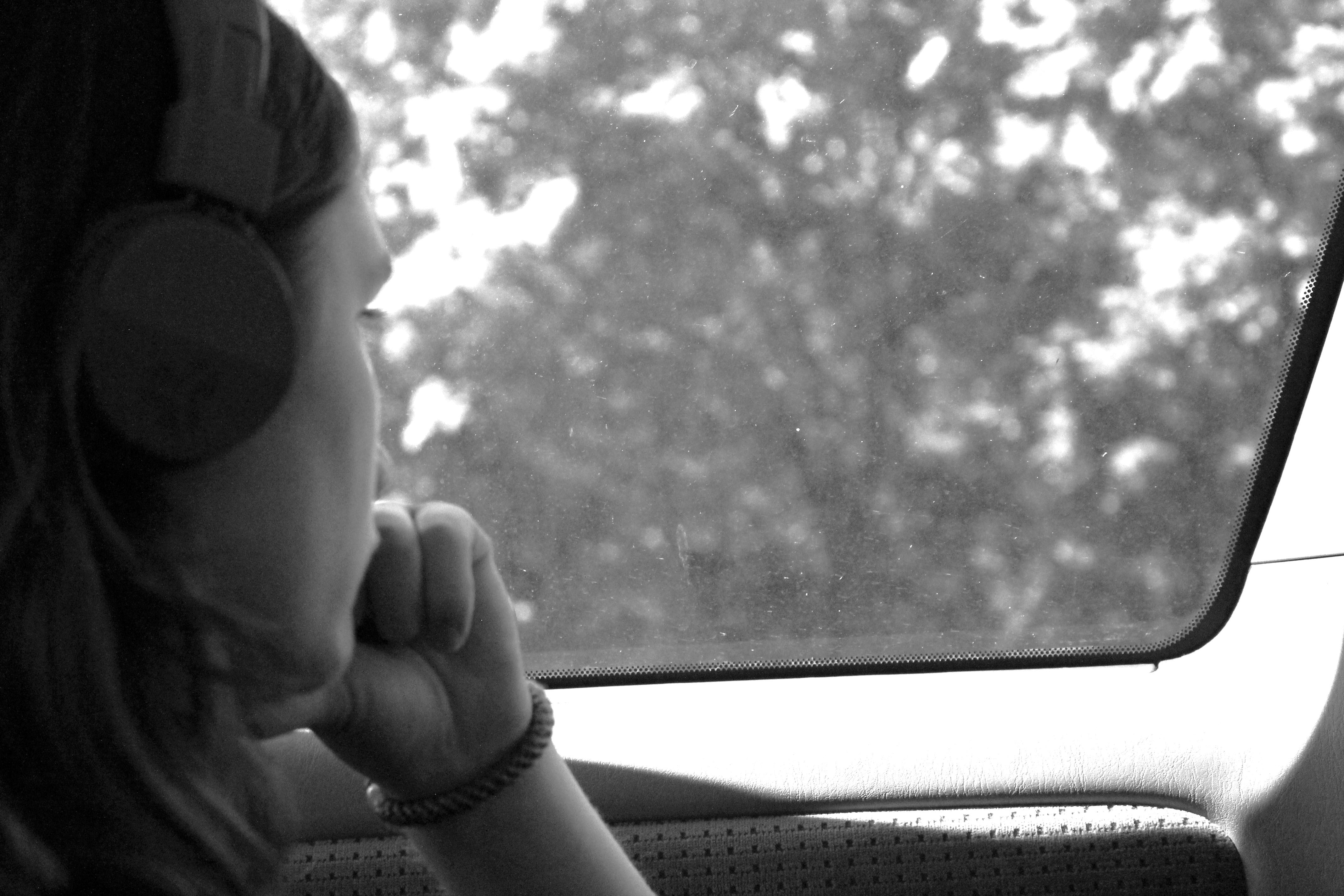 young person looking out the window of a car with headphones on, grayscale