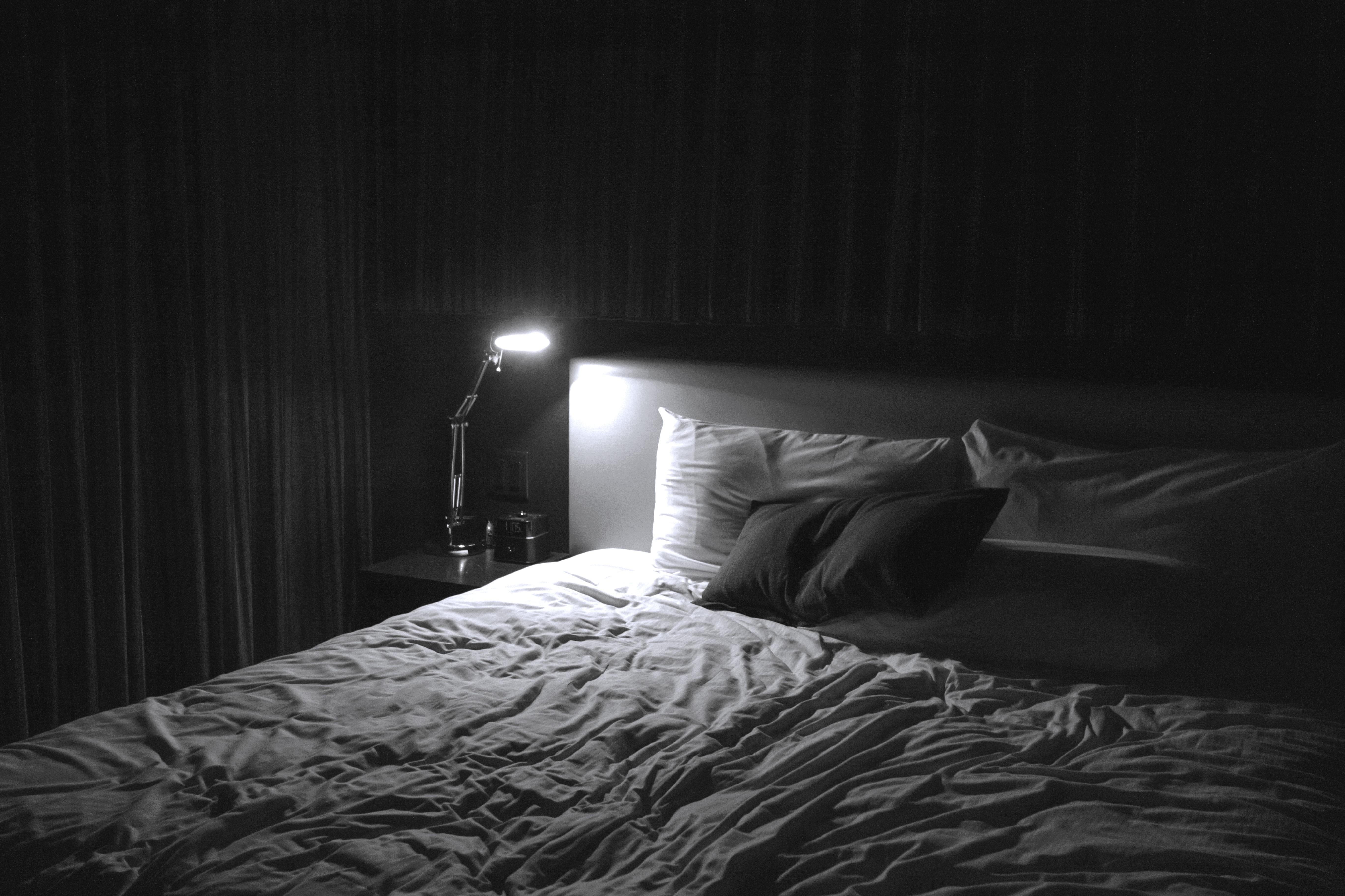 a black and white image of a dark bedroom with a lap shining on the beside table