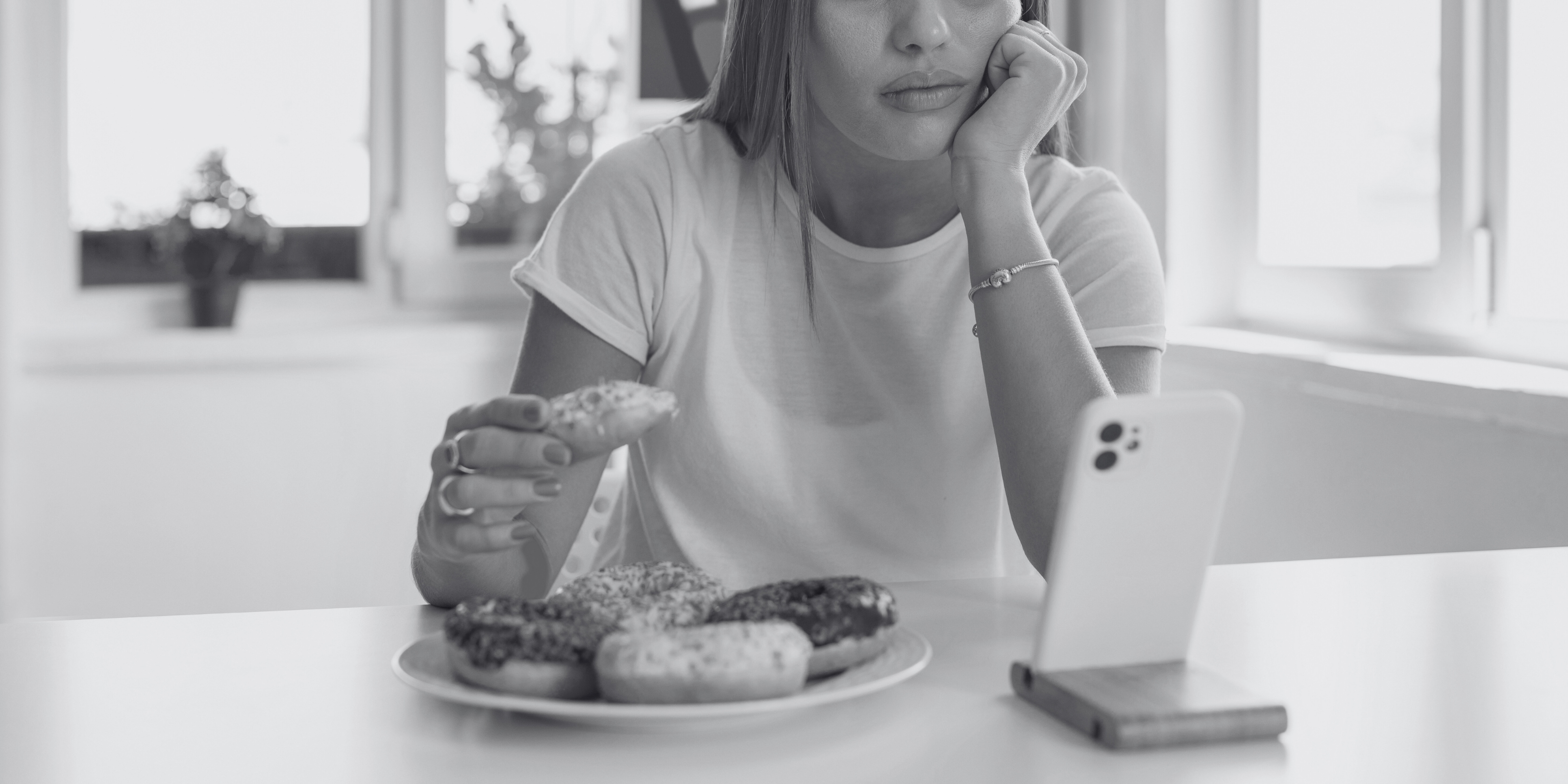 woman eating a donut looking sad and watching phone
