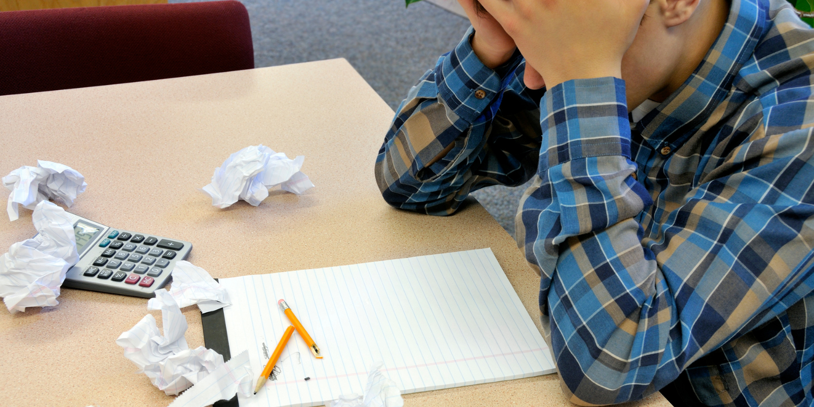 frustrated young man with his head in his hands sitting at a desk