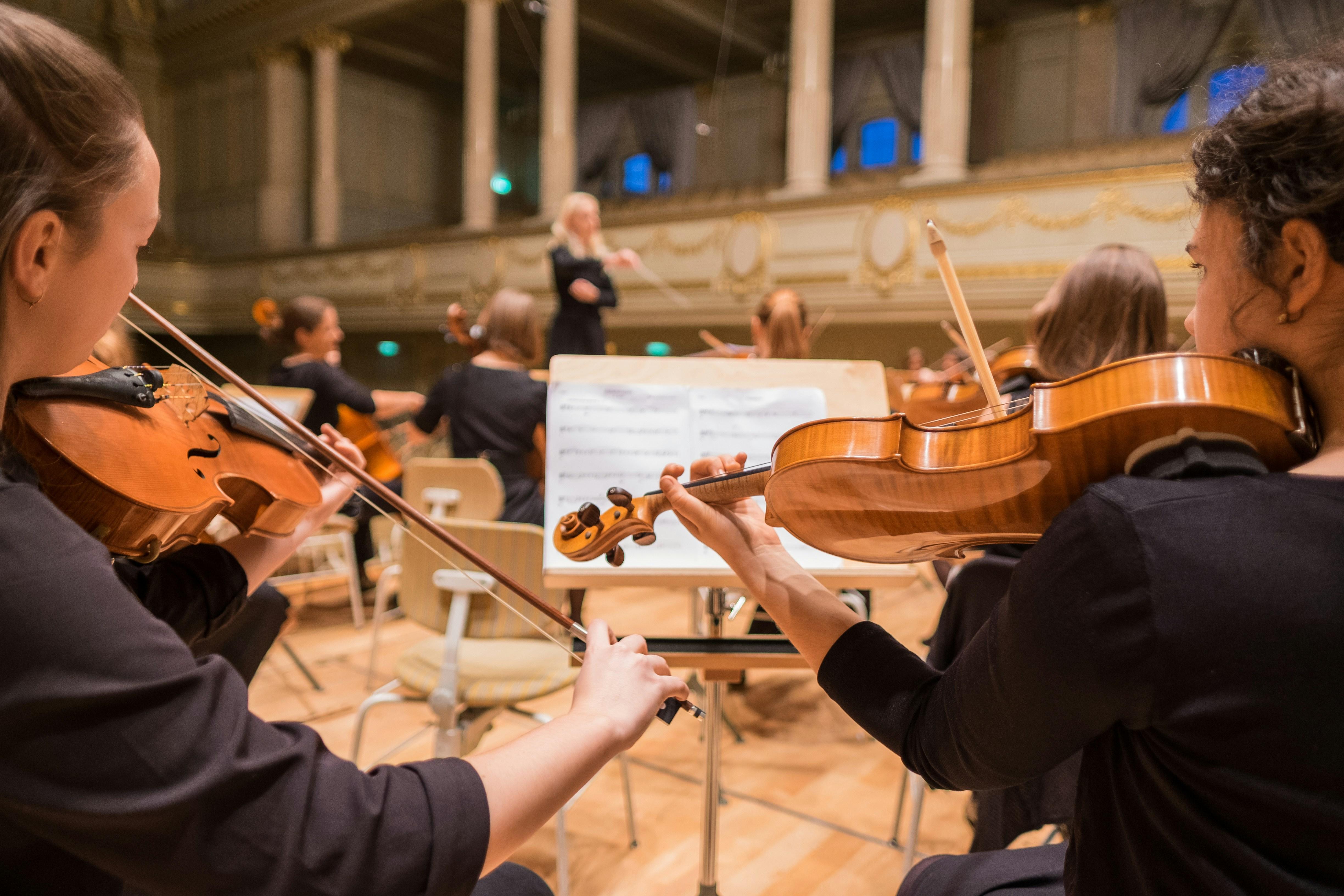 two young women playing violin in an orchestra with a stand of sheet music in front of them