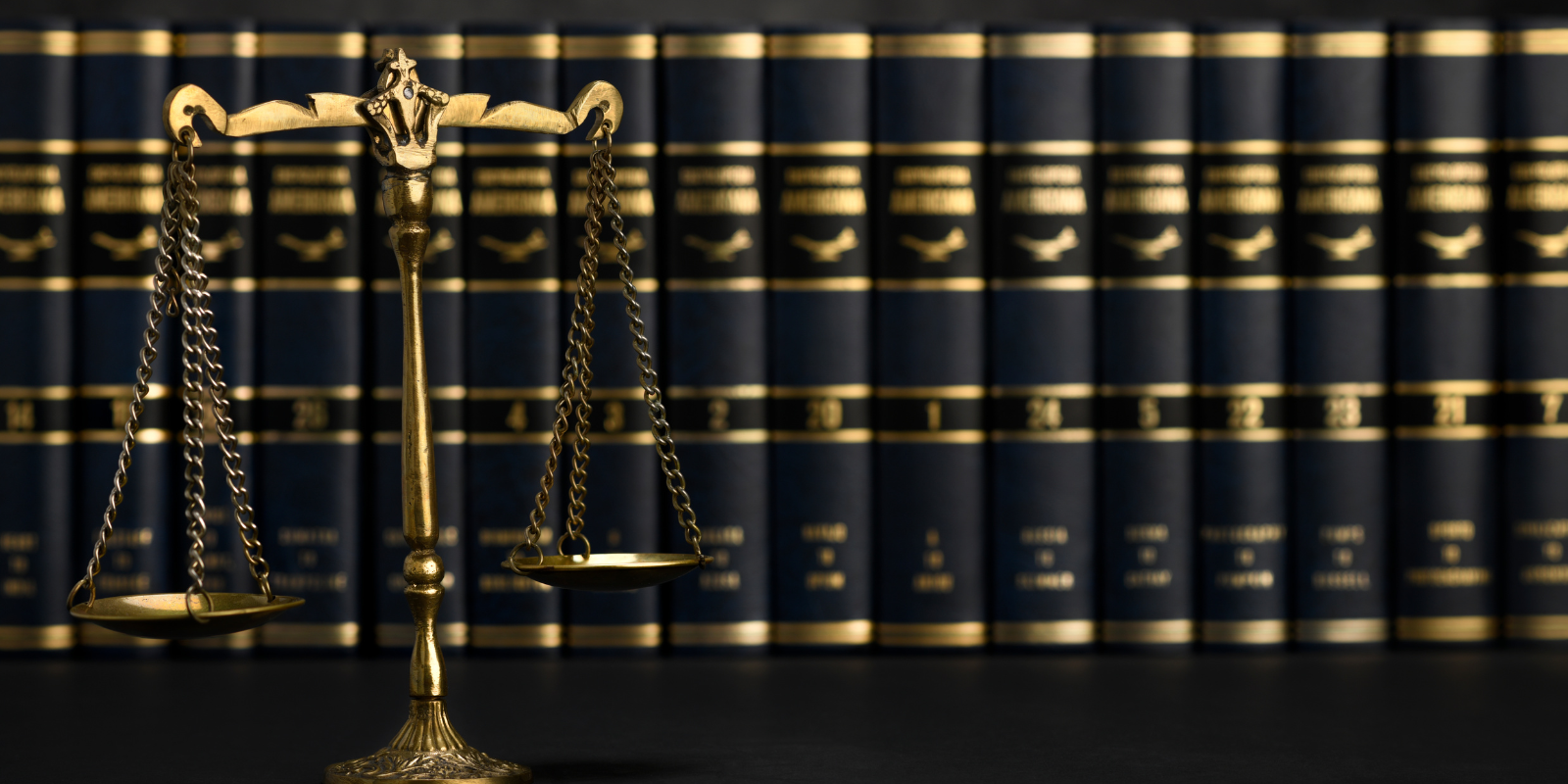 a justice scale in front of a bookshelf of books with black covers