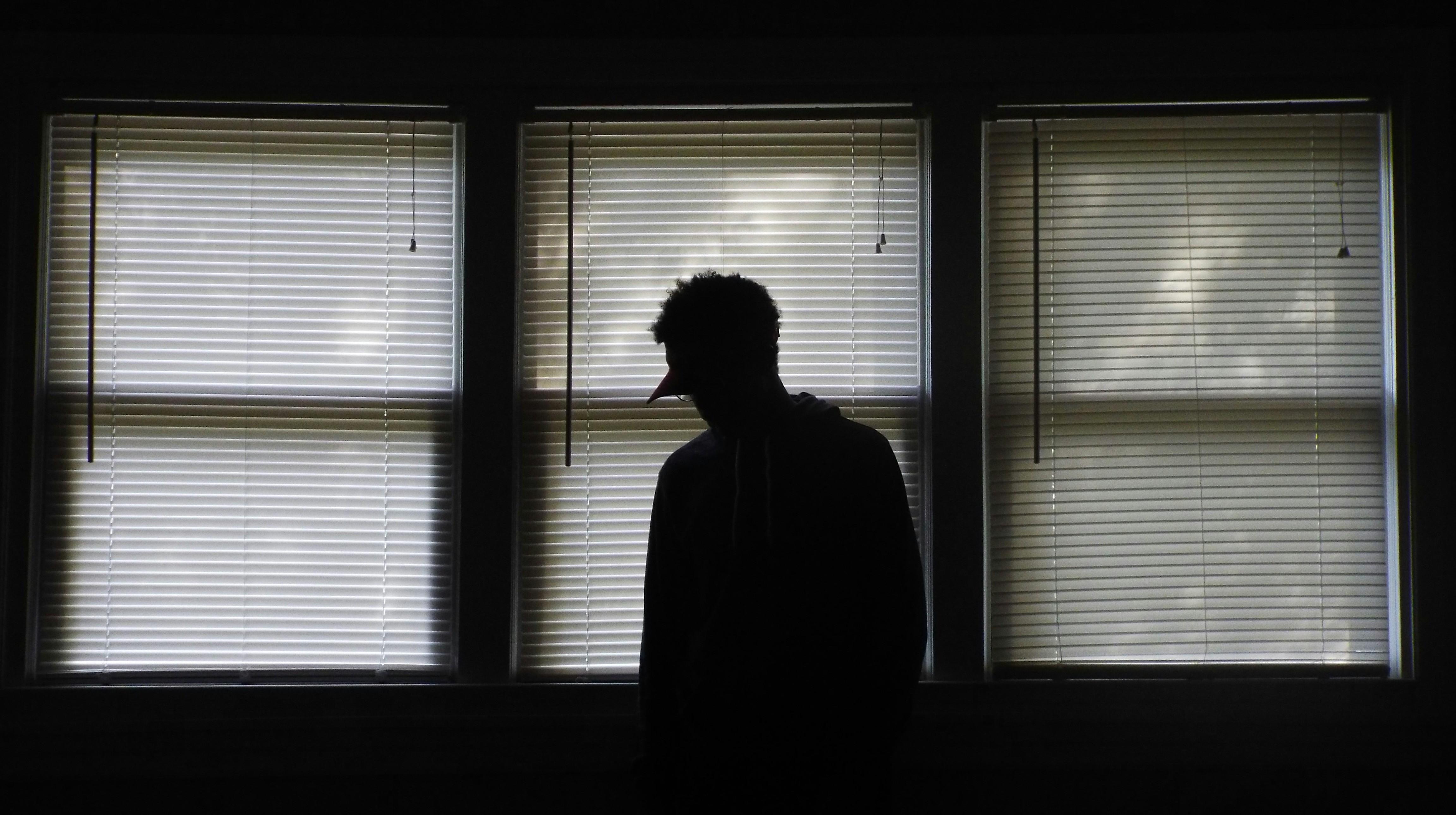 silhouette of someone standing in a dark room in front of 3 windows 