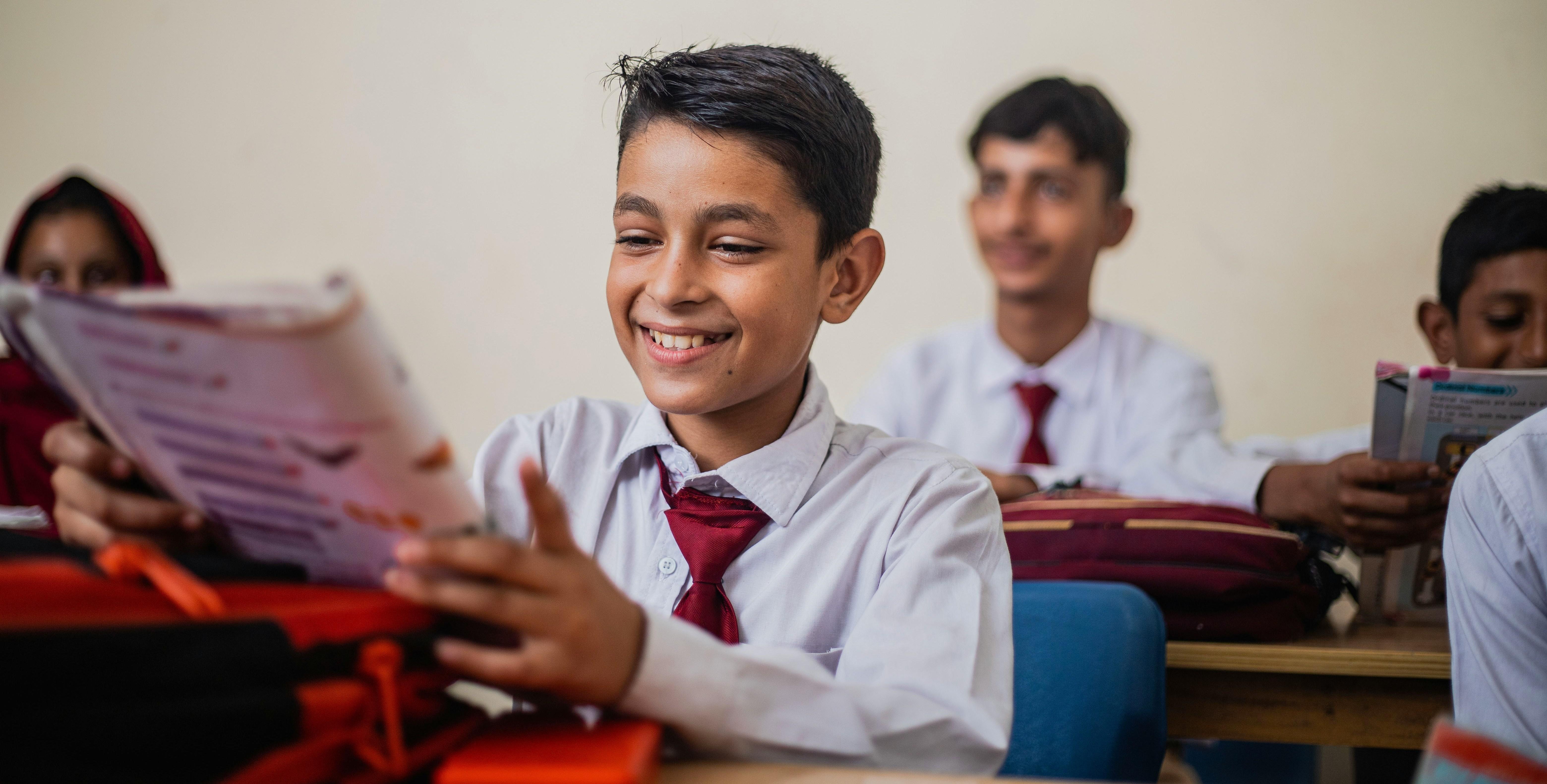 pakistani school boy in a uniform sitting in a classroom looking at a workbook
