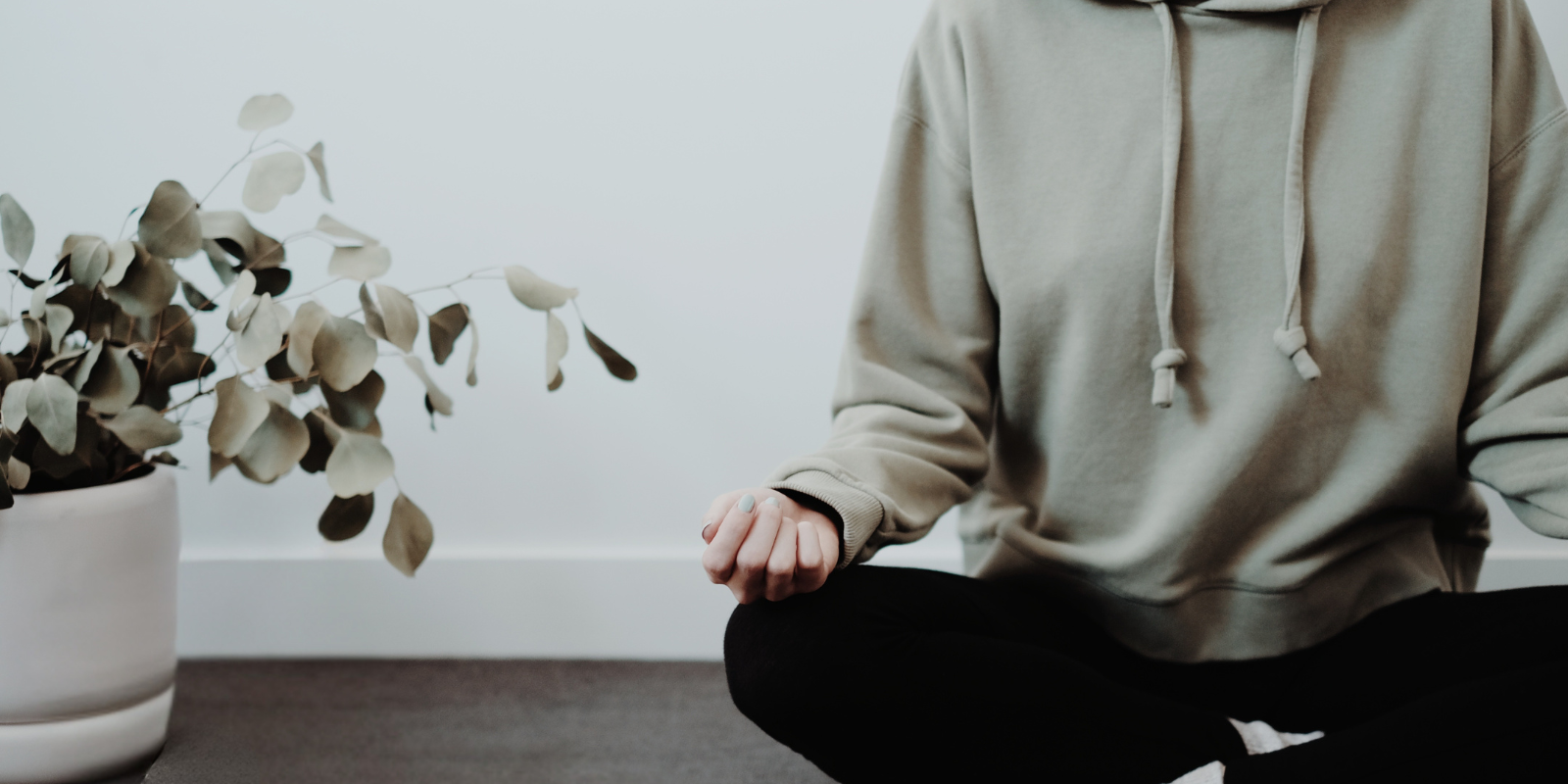 young woman in a green hoodie sitting on the floor meditating 
