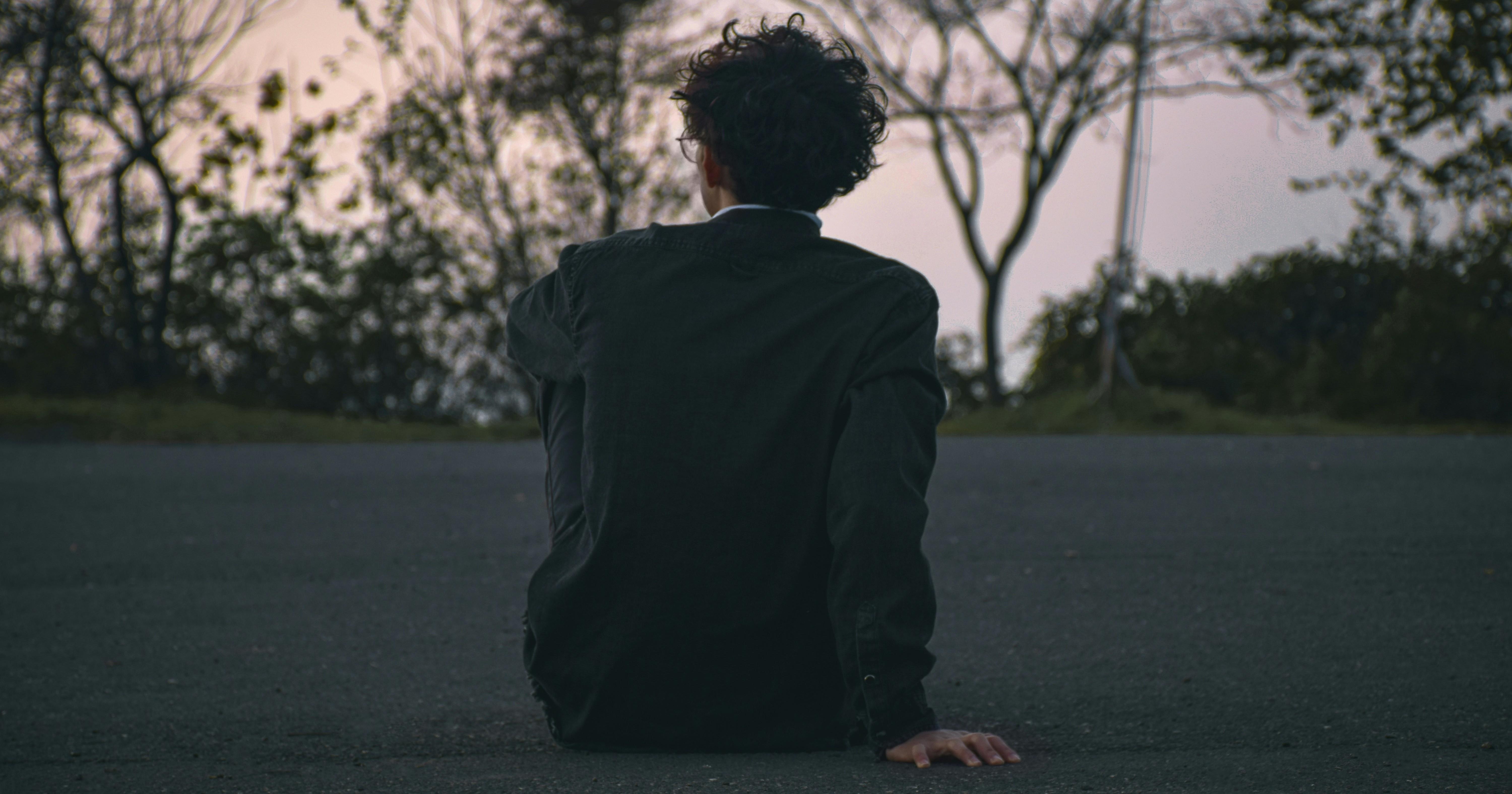 young boy sitting on the concrete facing away from the camera at sunset