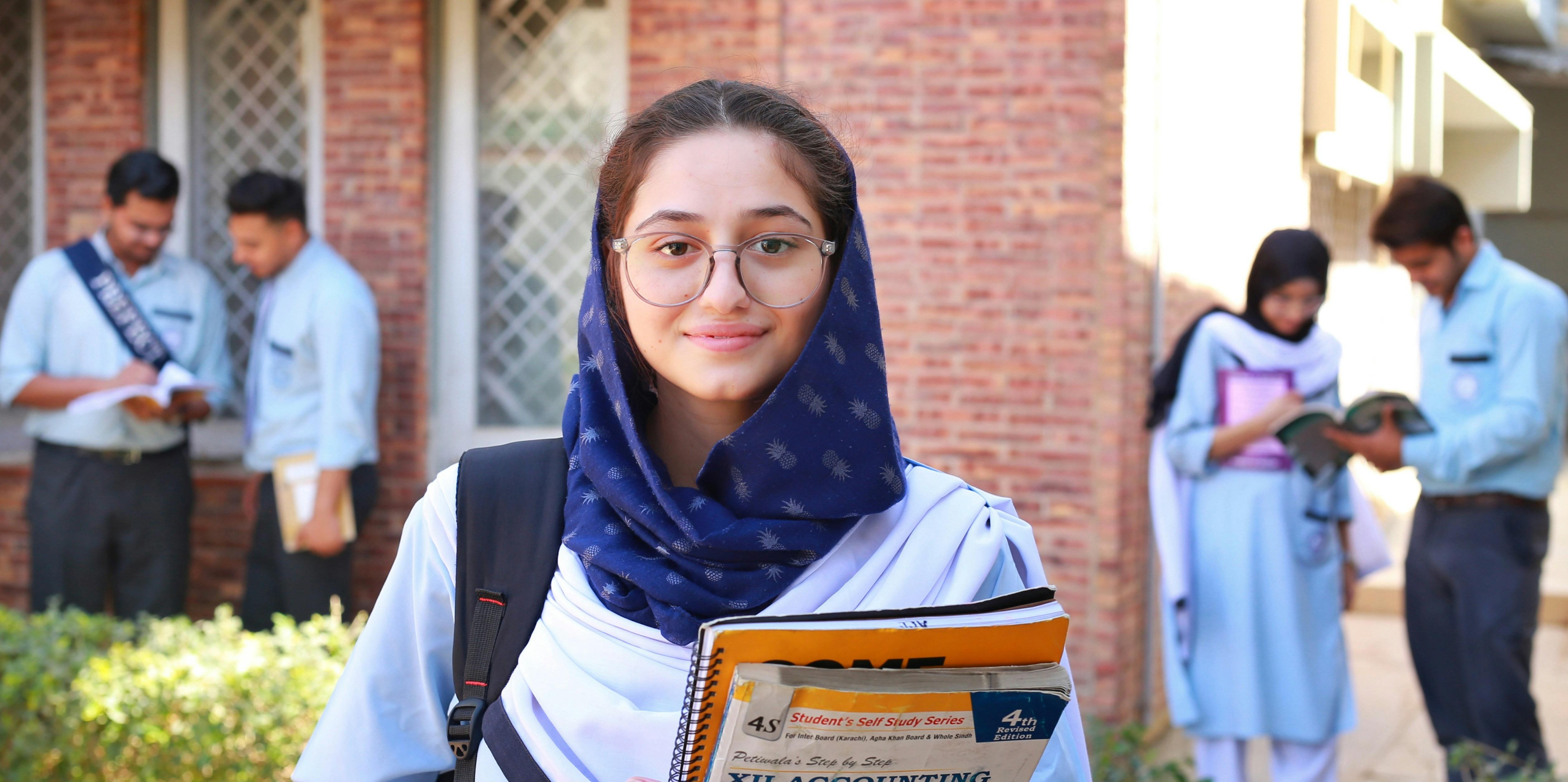 female student with a backpack looking at the camera and smiling holding a stack of books