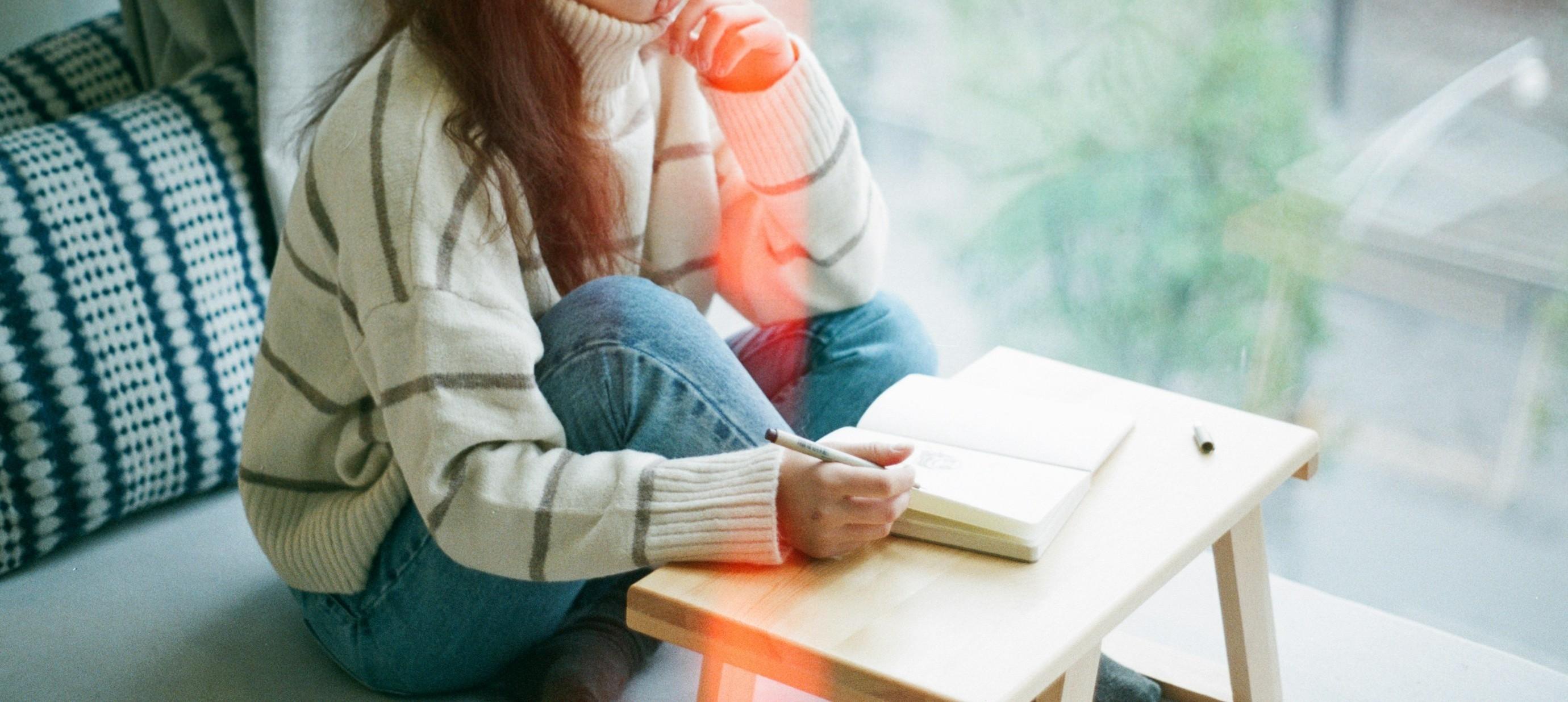young woman in a stripped sweater sitting on the couch writing in a notebook
