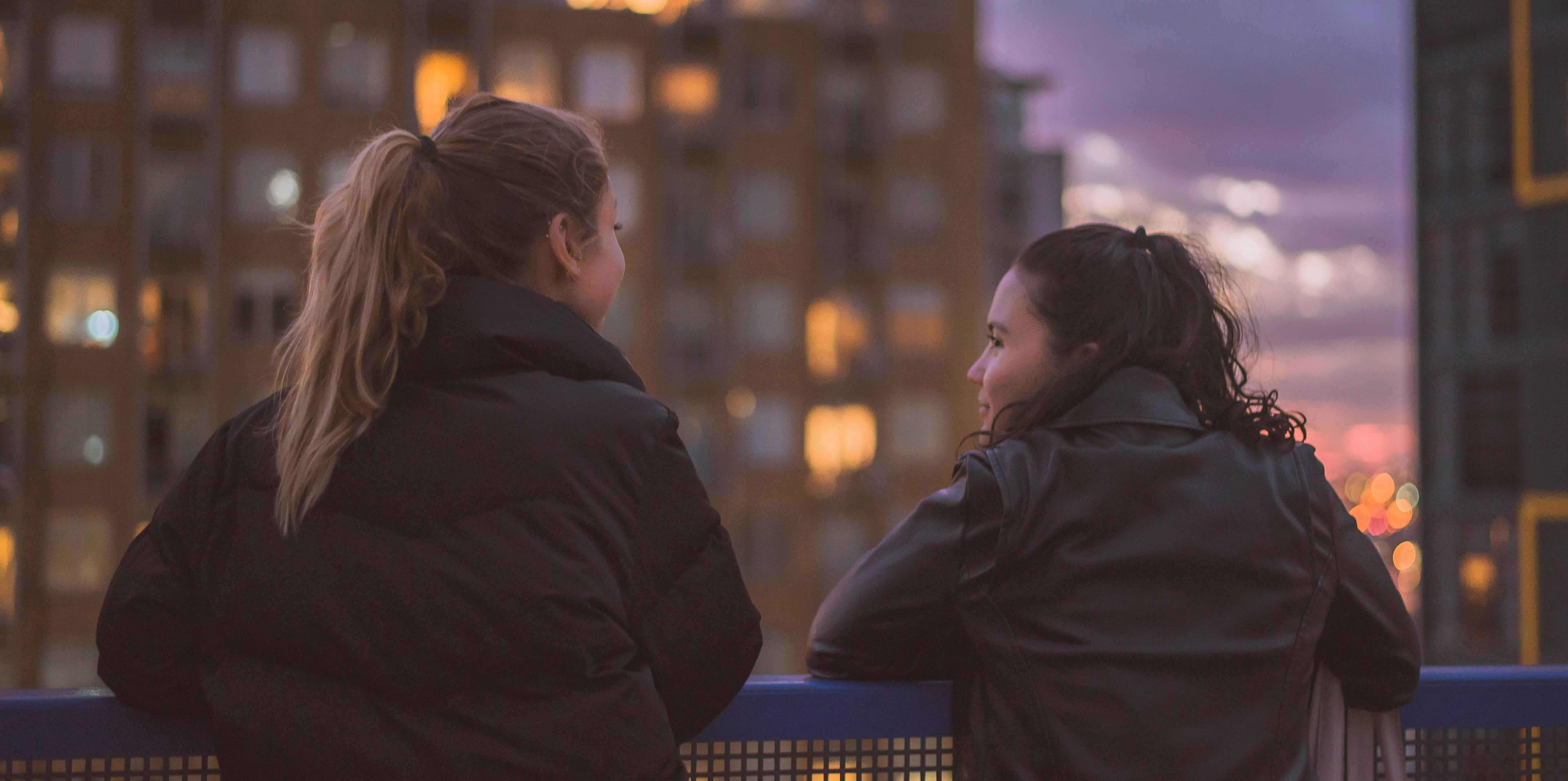 two young women on a roof overlooking the city one of them looking at the other