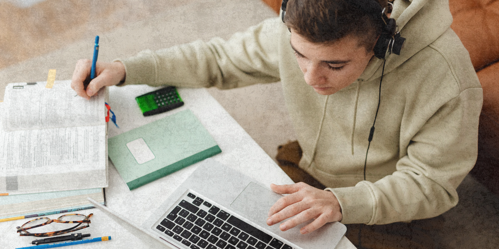 Teen Boy typing on laptop and referencing a book