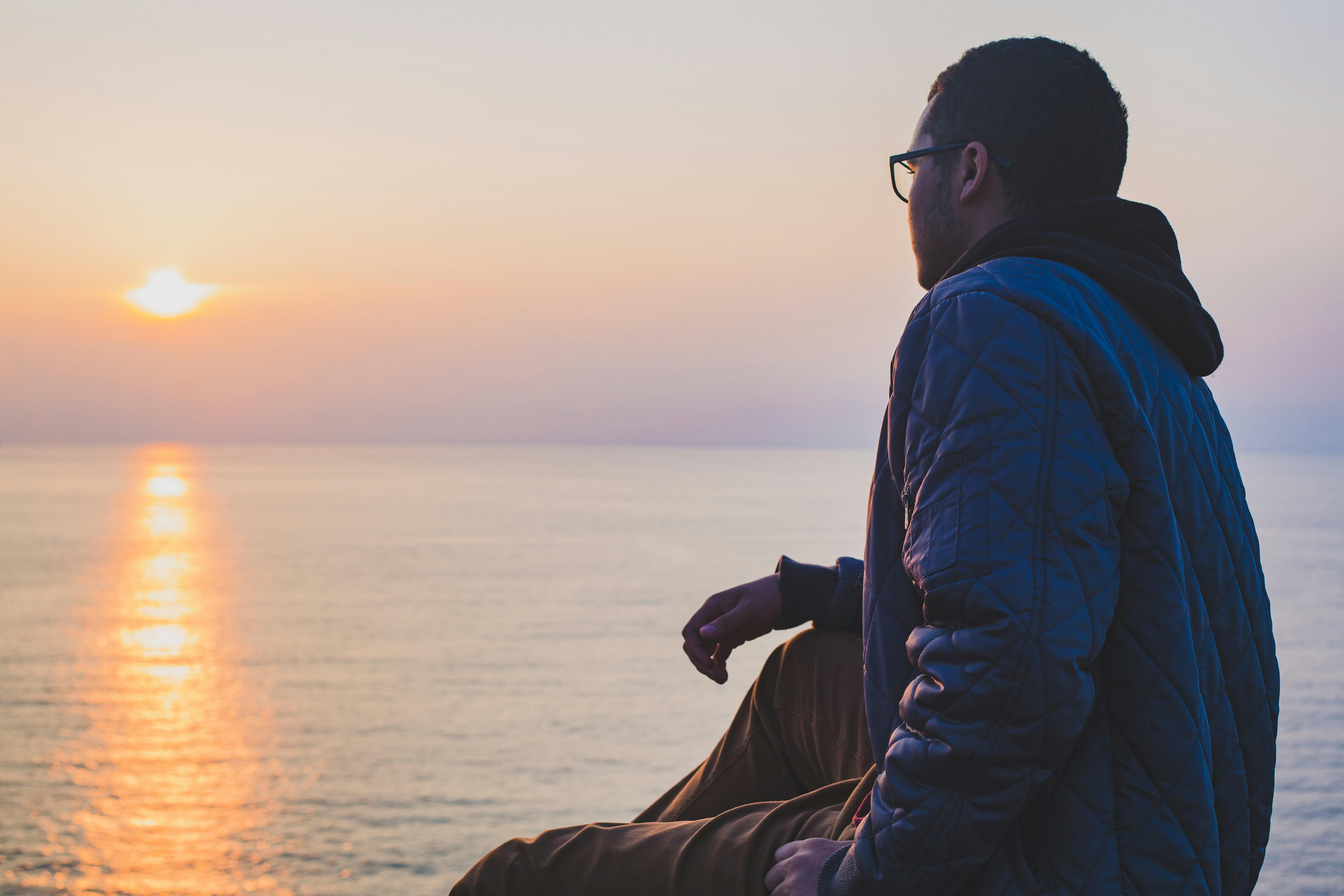 A man looking out at a sunrise over water.