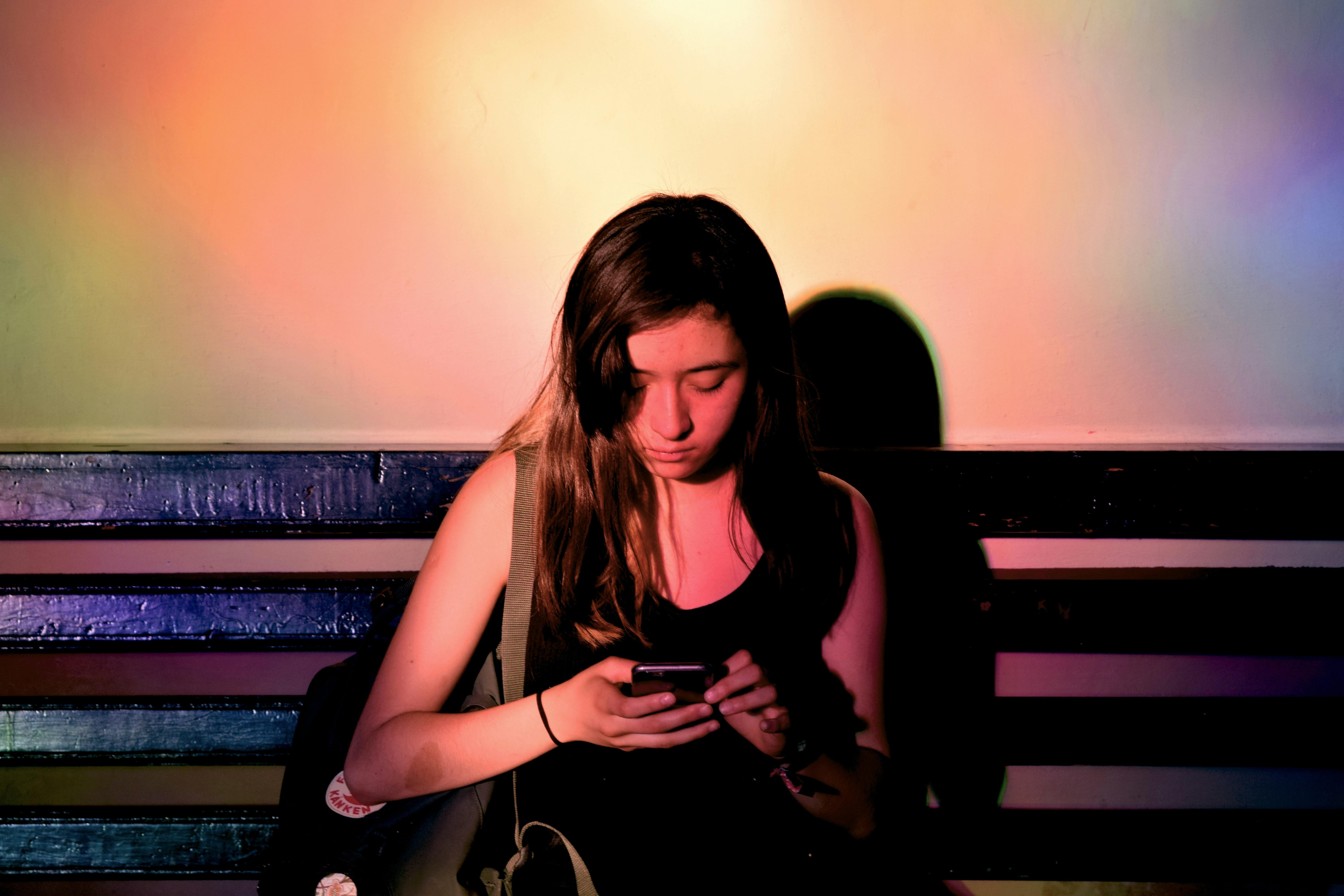 A young girl sitting on a bench looking at her phone. 