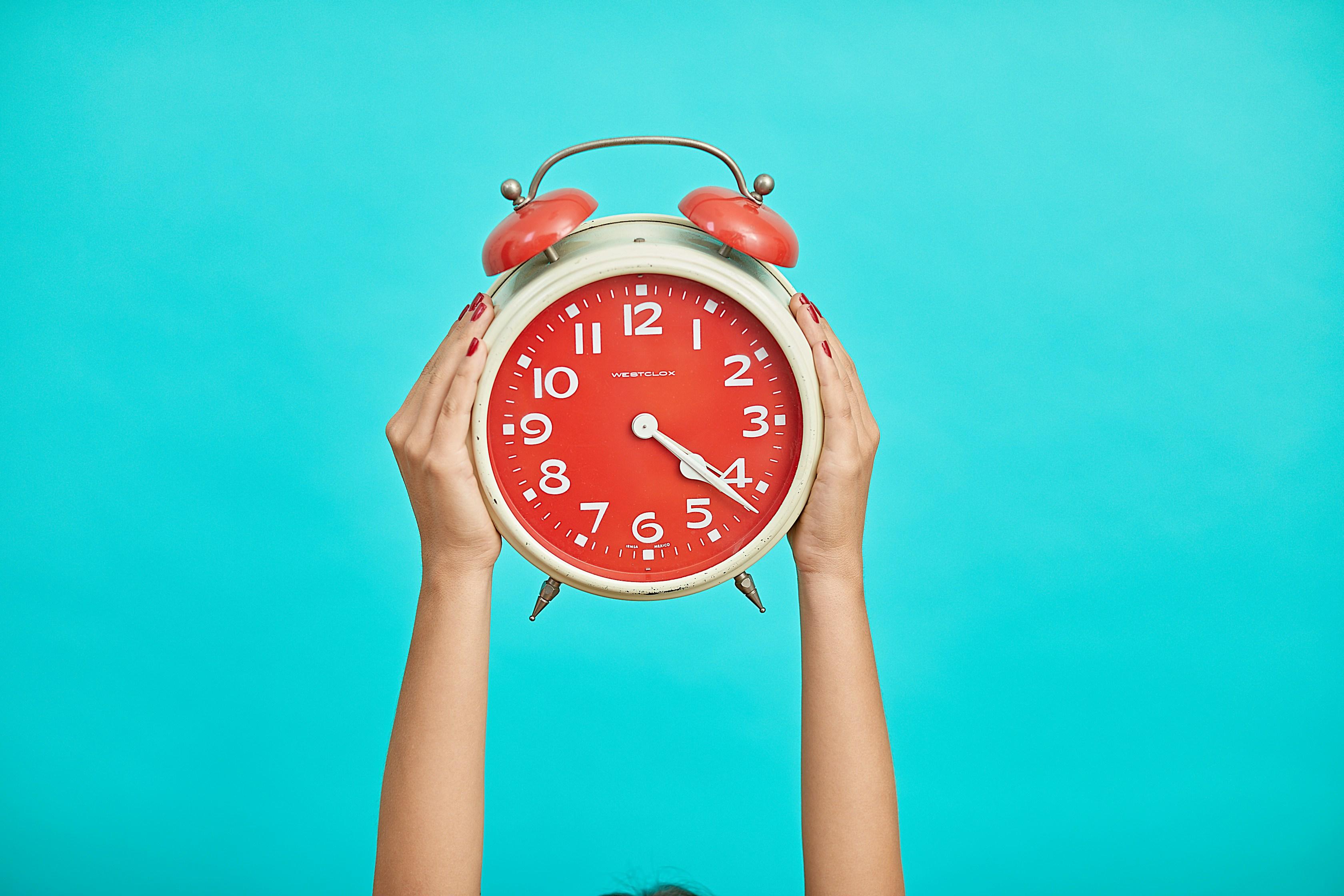 Hands holding up an alarm clock on a blue background