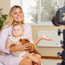 A woman with a child on her lap speaking to a camera on a tripod