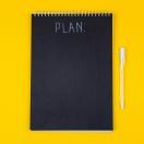 a black notebook that says "Plan" on a yellow background