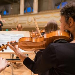 two young women playing violin in an orchestra with a stand of sheet music in front of them