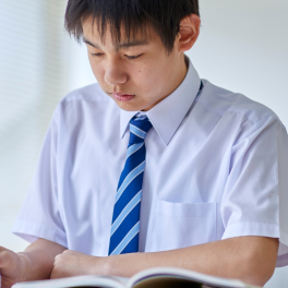 a teen male student wearing a uniform writing with a pen in a workbook