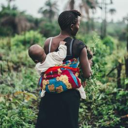 a mother walking with a child strapped to her back