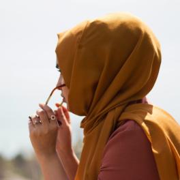 a young woman wearing an orange hijab, putting on sunglasses