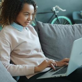 a young woman sitting on a couch typing on a laptop