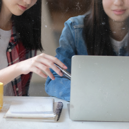 two young women sitting at a desk looking at a laptop