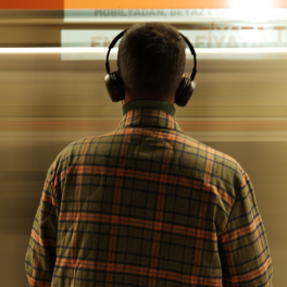 young man standing in front of moving train wearing headphones