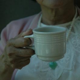 an elderly woman holding a white teacup