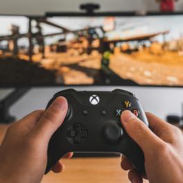 hands holding up xbox controller in front of a monitor displaying a video game