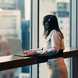 young woman looking out the window in a high rise office as she works on her laptop