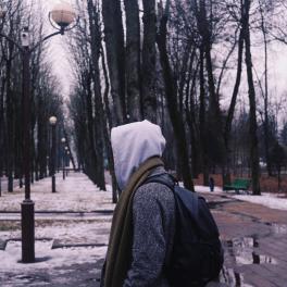 young man walking through a park with his hood up