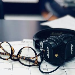 headphones, glasses and a calendar sitting on a desk