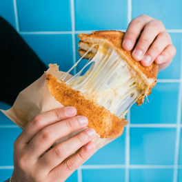 A toasted cheese sandwich being pulled apart on a blue background.