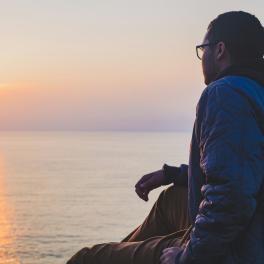 A man looking out at a sunrise over water.