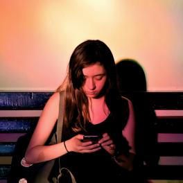 A young girl sitting on a bench looking at her phone. 