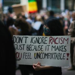 A woman in a mask holding a sign that reads 'Don't ignore racism just because it makes you feel uncomfortable'