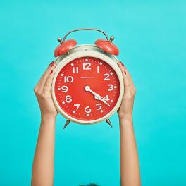 Hands holding up an alarm clock on a blue background