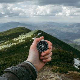 a hand holding out a compass over a mountain range