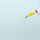 an image of a hand holding a syringe filled with a yellow liquid