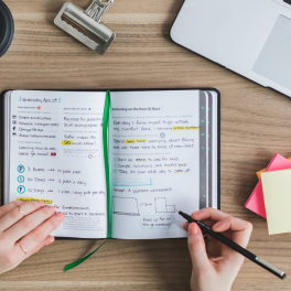 Flat lay image of study materials and a person writing in a planner