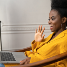 black woman on a video call waving at a laptop