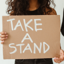 a woman holding a cardboard sign that reads "take a stand"